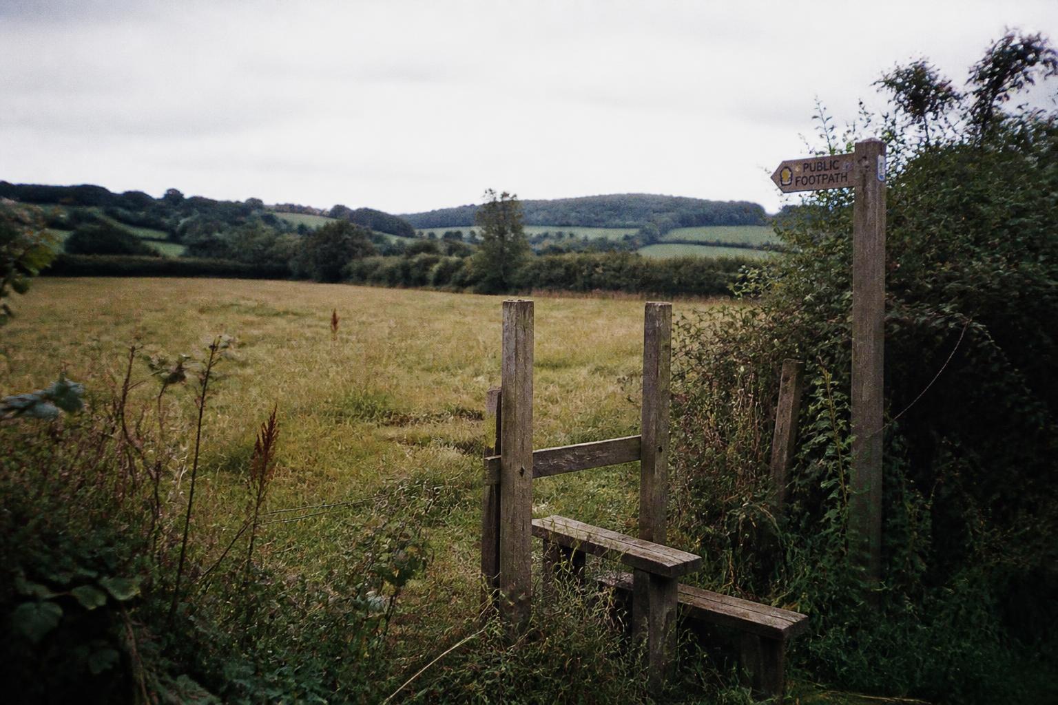 A public footpath sign leading into a green meadow with hills beyond