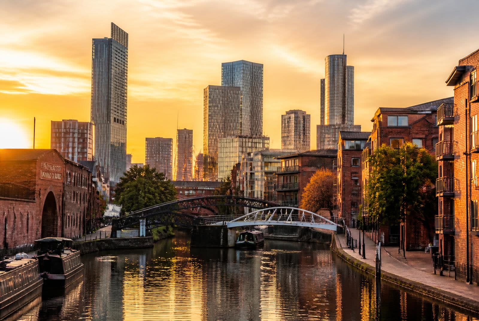 Manchester skyline at golden hour seen across a canal with red brick warehouses